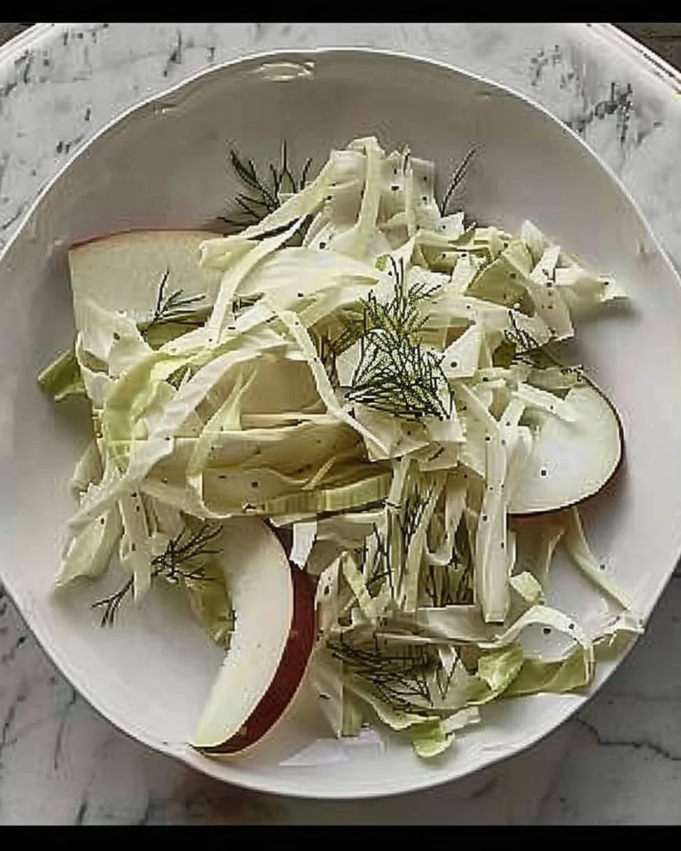 Fennel, apple, and cabbage slaw salad in a bowl with fresh ingredients